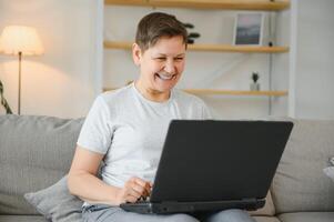 technologie, gens et la communication concept - content Sénior femme avec tablette PC ordinateur ayant vidéo bavarder à maison. moderne âge moyen Années 50 grand-mère asseoir se détendre sur canapé dans vivant pièce en utilisant portable. photo