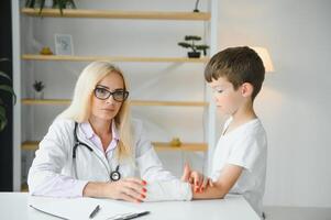 médecin examine un blessé main une peu garçon dans Bureau photo