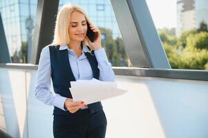 femme d'affaires avec téléphone près du bureau. portrait d'une belle femme souriante dans des vêtements de bureau de mode parlant au téléphone tout en se tenant à l'extérieur. communication téléphonique. image de haute qualité. photo