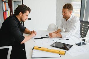 deux Jeune architectes avec plans de une maison permanent dans bureau, en parlant. photo