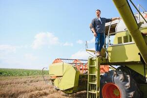 moissonneuse machine chauffeur escalade dans une taxi à récolte le sien blé champ. agriculteur avoir dans combiner sur échelle en portant balustrade. agronome. propriétaire de ranch après récolte travail photo