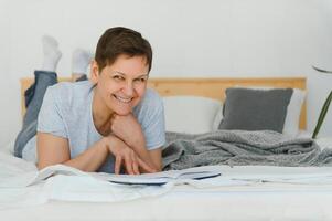 milieu âge blond femme en train de lire livre mensonge sur le lit à maison. photo