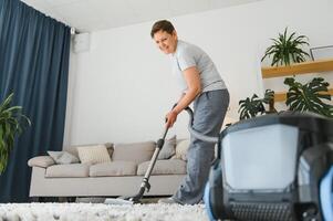 portrait de Sénior femme avec vide nettoyeur à l'intérieur à maison, aspirer photo