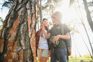 garçon et fille avec sacs à dos à la recherche examiner arbre écorce par grossissant verre tandis que explorant forêt la nature et environnement sur ensoleillé journée pendant Extérieur écologie école leçon. photo