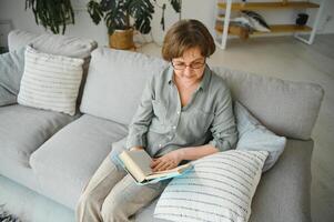 vieux Dame séance sur canapé et profiter intéressant roman Stock photo