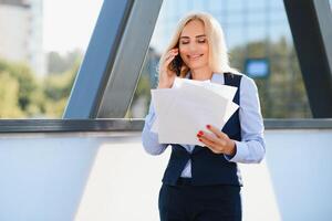 femme d'affaires avec téléphone près du bureau. portrait d'une belle femme souriante dans des vêtements de bureau de mode parlant au téléphone tout en se tenant à l'extérieur. communication téléphonique. image de haute qualité. photo