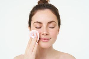 image de Jeune femme prise de sa maquillage avec coton tampons, en utilisant faciale nettoyant, nettoyage sa visage avec soin de la peau traitement, permanent plus de blanc Contexte photo