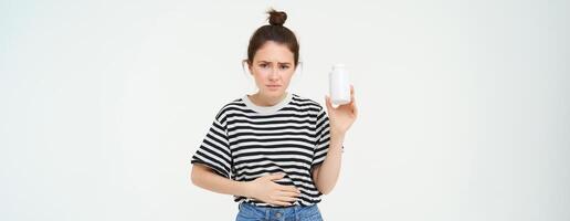 femme prend analgésiques, pilules de estomac mal, menstruel douleur, détient main sur ventre, spectacles bouteille avec comprimés, des stands plus de blanc Contexte photo