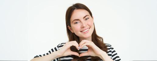 portrait de souriant, content petite amie spectacles cœur avec mains et à la recherche avec se soucier à caméra, Express sa l'amour ou affection, comme produit, permanent plus de blanc studio Contexte photo