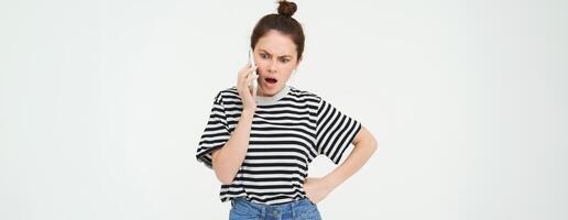 image de brunette femme argumentant, en criant sur Téléphone, ayant un argument sur mobile téléphone, permanent plus de blanc Contexte photo