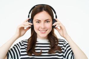 portrait de femme, souriant, portant sans fil écouteurs, écoute musique, en train d'étudier dans écouteurs, permanent isolé plus de blanc Contexte photo