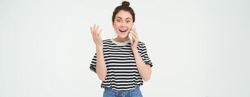 portrait de excité femme réponses téléphone appel, réagit étonné à magnifique nouvelles reçu plus de le Téléphone, permanent plus de blanc Contexte photo