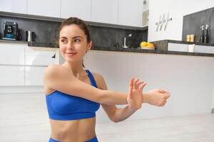 magnifique et en forme femme Est-ce que faire des exercices à maison, s'étire sa bras, Est-ce que réchauffer avant formation des exercices, porte soutien-gorge de sport, est assis sur caoutchouc yoga tapis photo