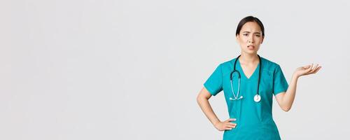 COVID-19 [feminine, soins de santé ouvriers, pandémie concept. frustré et agacé asiatique femelle médecin, infirmière dans gommages élever un main et à la recherche interrogé et énervé, se plaindre quelque chose photo