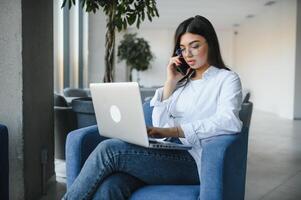 Jeune charmant femelle pigiste en utilisant portable ordinateur pour distance emploi tandis que séance dans moderne café magasin intérieur, magnifique caucasien femme travail sur net-book pendant Matin petit déjeuner dans café bar photo