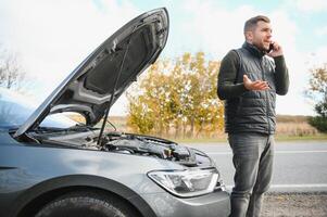 une homme appels une téléphone nombre à parler à une mécanicien. le voiture cassé vers le bas sur le bord de la route. le concept pour réparer, aider, problème, réparation. flou Contexte. photo