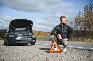 homme avec cassé voiture dans le milieu de le route. photo