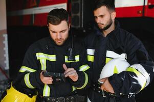 portrait de deux sapeurs pompiers dans Feu combat opération, pompier dans protecteur Vêtements et casque en utilisant tablette ordinateur dans action combat photo