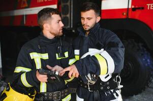 portrait de deux sapeurs pompiers dans Feu combat opération, pompier dans protecteur Vêtements et casque en utilisant tablette ordinateur dans action combat photo