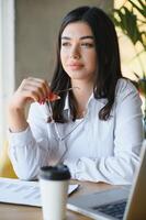 Jeune charmant femelle pigiste en utilisant portable ordinateur pour distance emploi tandis que séance dans moderne café magasin intérieur, magnifique caucasien femme travail sur net-book pendant Matin petit déjeuner dans café bar photo