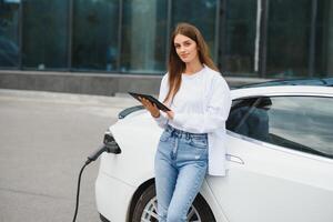 femme près de la voiture électrique. véhicule chargé à la borne de recharge. photo