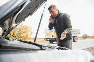 homme avec cassé voiture dans le milieu de le route. photo