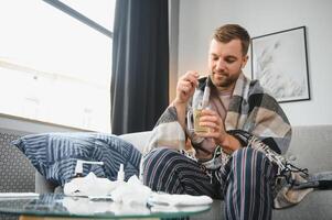 Jeune malade barbu européen homme à Accueil sur gris canapé avec couverture. maladie, protection, corona virus, virus, maladie, grippe photo