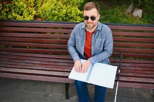 aveugle homme en train de lire livre sur banc dans parc photo