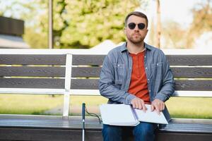 aveugle homme en train de lire livre sur banc dans parc photo