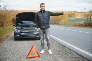 une Jeune homme avec une noir voiture cette cassé vers le bas sur le route, copie espace. photo