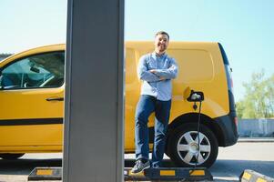 beau barbu gars près le sien Nouveau moderne électrique voiture à le mise en charge station photo