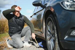 homme avec cassé vers le bas voiture plat pneu dans le milieu de le rue photo