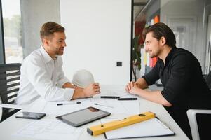 deux Jeune architectes avec plans de une maison permanent dans bureau, en parlant. photo