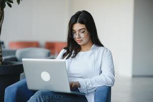 belle femme caucasienne rêvant de quelque chose tout en étant assise avec un net-book portable dans un café-bar moderne, jeune charmante pigiste pensant à de nouvelles idées pendant le travail sur un ordinateur portable photo