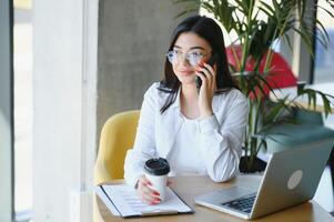 belle femme caucasienne rêvant de quelque chose tout en étant assise avec un net-book portable dans un café-bar moderne, jeune charmante pigiste pensant à de nouvelles idées pendant le travail sur un ordinateur portable photo