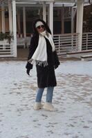 une blond fille dans une blanc tricoté chapeau, une longue écharpe et une fourrure manteau des promenades par le hiver ville. une femme des promenades dans le neige. hiver dehors. photo