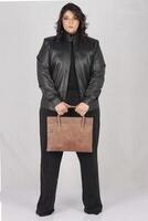une femme dans une noir cuir veste et noir un pantalon avec marron cuir main sac photo