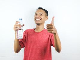 asiatique homme permanent souriant et montrer du doigt à minéral l'eau bouteille, pouce en haut photo