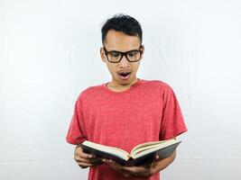 portrait de un asiatique homme avec une sous le choc expression tandis que en train de lire une livre. photo