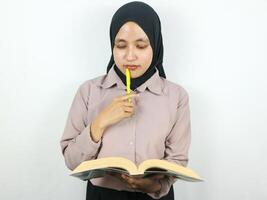 portrait magnifique asiatique femme dans hijab en portant livre et stylo, en pensant à propos quelque chose. photo