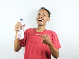 asiatique homme permanent souriant et montrer du doigt à minéral l'eau bouteille, pouce en haut photo
