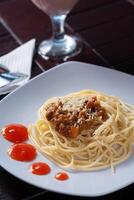 spaghetti bolognaise avec fromage saupoudré est mis sur une blanc assiette avec une en bois Contexte photo