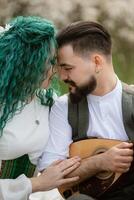 une barbu jeune marié pièces une à cordes instrument et une fille est assis dans une printemps Prairie photo