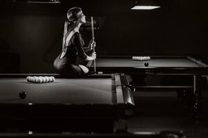 une fille avec une bandeau et une queue dans sa mains est séance sur une table dans une billard club.russe billard. noir et blanc photo