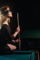 une fille avec une bandeau et une queue dans sa mains est séance sur une table dans une billard club.russe billard photo