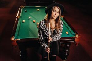 une fille dans une chapeau dans une billard club avec une queue dans sa mains.billard Jeu photo