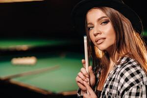 une fille dans une chapeau dans une billard club avec une queue dans sa mains.billard Jeu photo