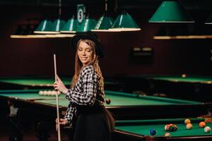 une fille dans une chapeau dans une billard club avec une queue dans sa mains.piscine Jeu photo