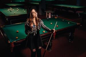 une fille dans une chapeau dans une billard club avec une queue dans sa mains.billard Jeu photo