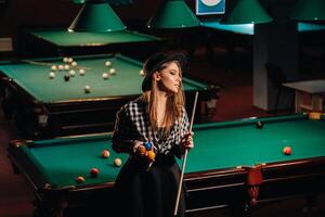 une fille dans une chapeau dans une billard club avec une queue dans sa mains.billard Jeu photo